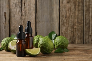 Photo of Bottles of essential oil and fresh bergamot fruits on wooden table. Space for text