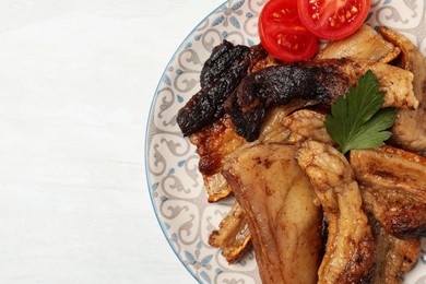 Photo of Tasty fried pork lard with parsley and tomatoes on white wooden table, top view