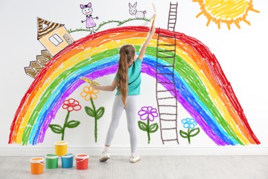 Little girl drawing her dreams on wall, back view