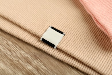 Beige apparel with blank clothing label on wooden table, closeup