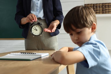 Teacher scolding pupil for being late in classroom, focus on alarm clock