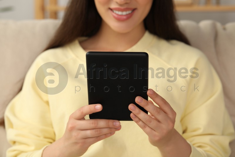Young woman using e-book reader indoors, closeup