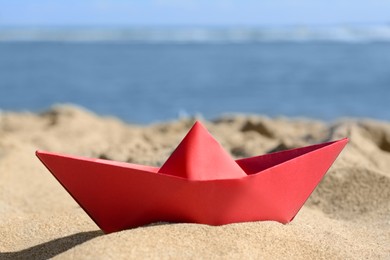 Red paper boat near sea on sunny day, closeup