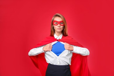 Confident businesswoman wearing superhero costume under suit on red background