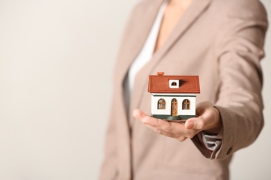 Female agent holding house model on light background, closeup. Home insurance
