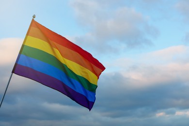 Bright LGBT flag against blue sky with clouds. Space for text