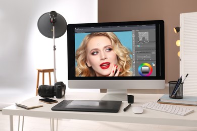 Retoucher's workplace. Computer with photo editor application, camera, smartphone and graphic tablet on table in studio