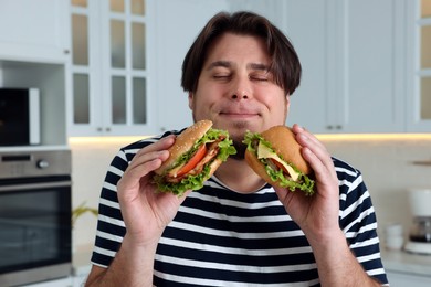 Happy overweight man tasty burgers in kitchen