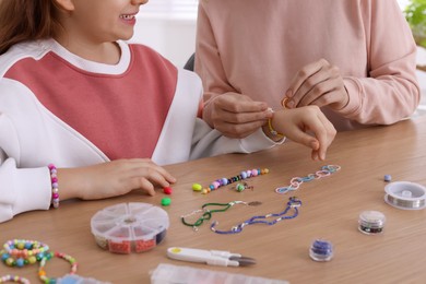 Mother with her daughter making beaded jewelry at home, closeup