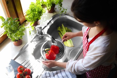 Photo of Woman washing fresh bell peppers in kitchen sink, above view