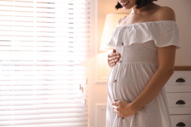 Pregnant young woman touching belly at home, closeup. Space for text