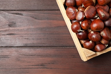 Fresh sweet edible chestnuts in crate on wooden table, top view. Space for text