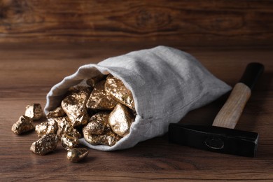 Overturned sack of gold nuggets and hammer on wooden table