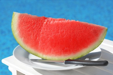 Slice of fresh juicy watermelon on white plate near swimming pool outdoors, closeup