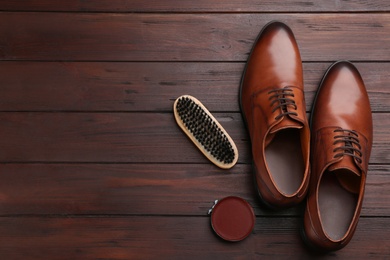 Flat lay composition with shoe care accessories and footwear on brown wooden background. Space for text