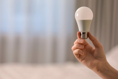 Woman holding fluorescent light bulb on blurred background, closeup with space for text. Saving energy concept