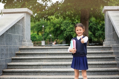 Cute school child with stationery near stairs in park