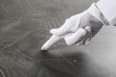 Person in white glove checking cleanliness of grey stone table, closeup