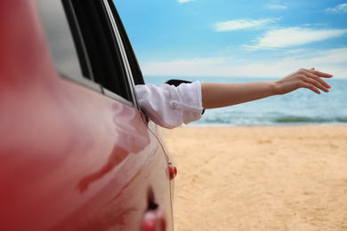 Woman waving from car on beach, closeup. Summer vacation trip