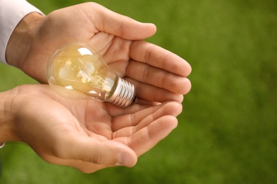 Man holding lamp bulb against green background. Space for text
