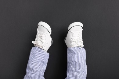 Photo of Little baby in stylish gumshoes on black background, top view