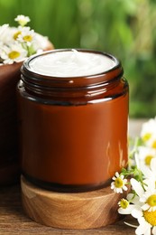 Jar of hand cream and chamomiles on wooden table, closeup