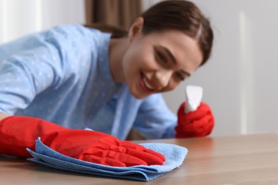 Young woman cleaning wooden table with rag at home, focus on hand