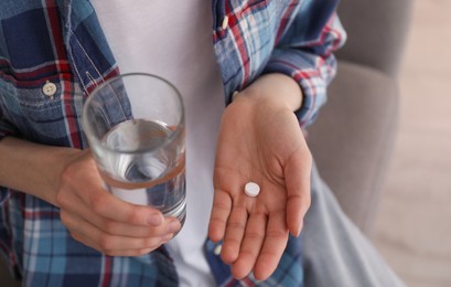 Young woman with abortion pill and glass of water indoors, closeup