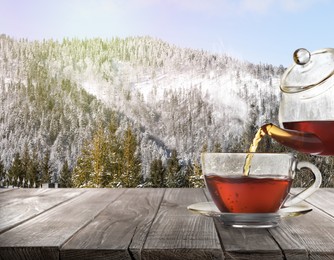 Pouring tea into glass cup on wooden table and beautiful winter landscape on background