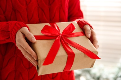 Woman holding Christmas gift box indoors, closeup