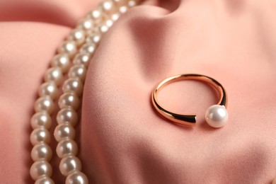 Elegant necklace and ring with pearls on pink silk, closeup
