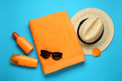 Photo of Beach towel, hat, sunglasses and sun protection products on light blue background, flat lay