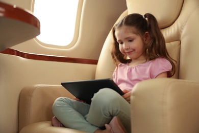 Cute little girl using tablet in airplane during flight