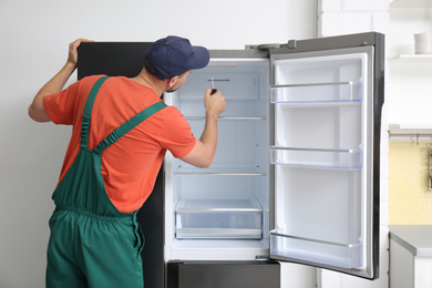 Male technician with screwdriver repairing refrigerator indoors