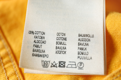 Clothing label with care symbols and material content on yellow jeans, closeup view