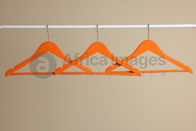 Photo of Orange clothes hangers on metal rail against beige background