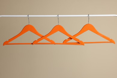 Orange clothes hangers on metal rail against beige background