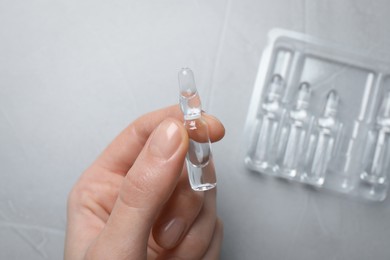 Woman holding pharmaceutical ampoule with medication at light grey table, top view