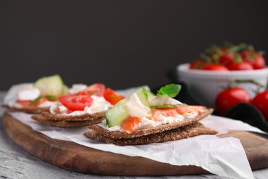 Tasty rye crispbreads with salmon, cream cheese and cucumber on wooden board, closeup