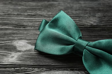 Stylish green satin bow tie on black wooden background, closeup