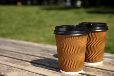 Takeaway cardboard coffee cups with plastic lids on wooden bench outdoors, space for text