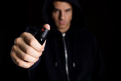 Man using pepper spray against black background, focus on hand. Space for text