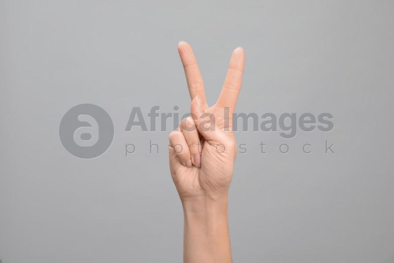 Photo of Woman showing number two on grey background, closeup. Sign language