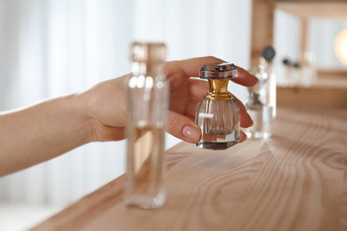Woman taking bottle of perfume from wooden shelf indoors, closeup