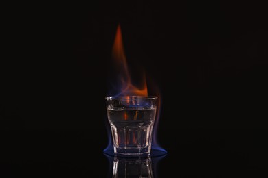 Flaming vodka in shot glass on black background