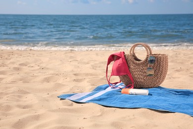 Blue striped beach towel with bag, swimsuit and accessories on sandy seashore, space for text