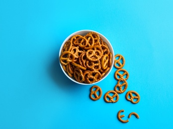 Delicious pretzel crackers in bowl on light blue background, flat lay