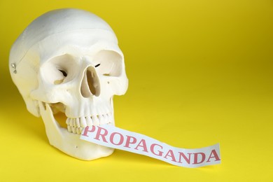 Photo of Information warfare concept. Human skull and paper card with word Propaganda on yellow background, space for text