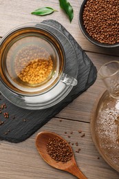 Cup of freshly made aromatic buckwheat tea and granules on wooden table, flat lay