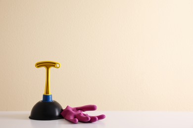 Plunger and rubber glove on white table against beige background. Space for text